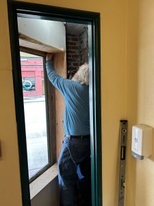 Bruce, volunteer, installing window and frame by Roxy's entry to house digital poster display